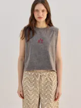 Musculosa crop de algodón con efecto acid wash en color lila, cuello redondo, hombreras marcadas y pequeño bordado central en el pecho.