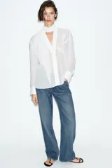 Blusa de tejido semitransparente con efecto arrugado, escote en pico y manga larga. Presenta un detalle decorativo frontal con estructura en forma de flor.