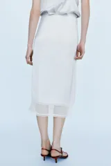 Falda midi de tiro medio, color blanco, confeccionada en hilatura de viscosa 100%, con detalle de aplicación de tejido combinado semitransparente con abertura en el bajo y cierre lateral con cremallera oculta.