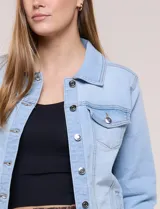 Campera de jean Baccini de color celeste claro, con cuello solapa, cierre frontal con botones metálicos, bolsillos en el pecho y ruedo con terminación desflecada.