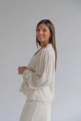 Blusa de color beige con cuello mao, cierre frontal con botones y mangas largas abullonadas. Presenta delicados bordados florales en la parte superior delantera.