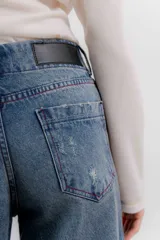 Pantalón de jean color naranja con tiro medio, diseño de pierna ancha y cinco bolsillos. Presenta costuras con pespuntes a contratono.