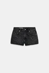 Shorts de denim negro con lavado oscuro, tiro alto, cinco bolsillos y bajo deshilachado. Presenta aplicaciones de brillos o tachas pequeñas dispersas por toda la parte delantera.