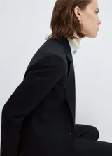 Blazer entallado de color negro, con solapas con muesca, hombros estructurados y cierre frontal de un botón. Presenta dos bolsillos de ribete delanteros, pinzas de entalle y una abertura posterior.