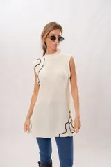 Chaleco largo color crema de tejido de punto con cuello alto y sisas amplias. Presenta un diseño de líneas negras irregulares en los bordes.