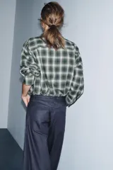 Camisa de corte oversize confeccionada en algodón, con estampado de cuadros en tonos verde, negro y blanco. Presenta cuello solapa, cierre frontal con botones, manga larga con puños y bajo asimétrico.