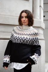 Sweater de lana con diseño de jacquard en la parte superior, cuello redondo, mangas largas y puños acanalados. Presenta un corte holgado con tajos laterales y un diseño ligeramente más corto en la parte delantera.