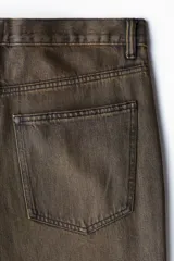 Jeans de corte relajado y pierna recta, confeccionados en denim de algodón rígido en color marrón con efecto desteñido y lavado desgastado. Presentan diseño clásico de cinco bolsillos, trabillas para cinturón y cierre frontal con botón y cremallera.