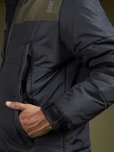 Campera acolchada con diseño de bloques de color en azul marino y azul oscuro, con capucha, cierre frontal y bolsillos laterales.
