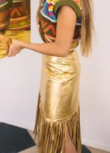 Falda midi de tiro alto, confeccionada en cuero dorado, de silueta ajustada con tajo lateral y flecos largos en el frente.