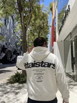 Canguro blanco con capucha, con gran estampado en la espalda en color negro que incluye texto y logotipos de la marca.