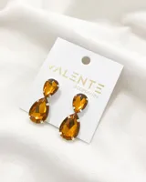 Par de aros colgantes con dos cristales facetados color ámbar engarzados en metal plateado. El cristal superior es más pequeño y tiene forma de lágrima invertida, mientras que el cristal inferior es más grande y tiene forma de lágrima.