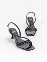 Sandalias de tacón medio modelo Loira, confeccionadas en cuero charol negro con tiras cruzadas cubiertas de strass. Tienen punta cuadrada, taco fino laqueado de 6,5 cm y tira ajustable al talón con hebilla.