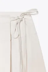 Falda tipo pareo color blanco, de tiro medio, con cierre lateral ajustable mediante lazada y bajo asimétrico.