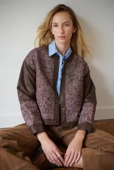 Chaqueta bomber color bordó con mangas de cuero sintético marrón y cuerpo de tweed con patrón de espiga. Cierre frontal con botones a presión y cuello redondo.