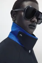 Chaqueta de Zara Woman Collection color negro, de cuello con solapa y manga larga. Cuenta con bolsillos delanteros ocultos en las costuras, cierre frontal con botones metálicos a presión y detalle de diseño asimétrico en azul en el cuello.