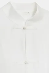 Camisa de estilo oriental confeccionada en mezcla de lyocell con acabado satinado. Presenta cuello redondo, manga larga con puños rectos, bolsillos de plastrón y cierre frontal mediante alamares.