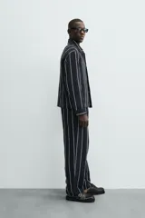 Pantalón de corte relajado, color azul marino, con rayas verticales blancas finas. Presenta cintura elástica ajustable con cordón interior y bolsillos laterales y traseros de plastrón.