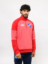 Buzo de entrenamiento Umbro del Club Nacional de Football, con diseño de medio cierre y cuello alto. Presenta cuerpo en tono rojo jaspeado y mangas en rojo liso, con el escudo del club y el logo de la marca en el pecho.