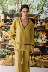 Blusa de manga larga color pistacho con escote en V ribeteado en color marrón oscuro. El tejido parece ser lino o una mezcla ligera, con un corte holgado.