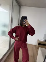 Conjunto de dos piezas color bordó, compuesto por un buzo de cuello redondo con mangas largas y un pantalón de corte holgado con cintura elástica.