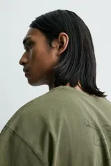 Camiseta de corte relajado, color verde oliva con efecto lavado. Presenta cuello redondo, manga corta y un gráfico estampado en la espalda.
