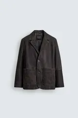 Blazer de corte relajado confeccionada en piel con acabado de ante. Presenta cuello con solapas de muesca, cierre frontal de dos botones, mangas largas y bolsillos de plastrón en la parte delantera. Destaca por sus costuras con efecto lavado que le otorgan un aspecto vintage.