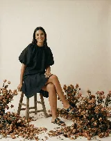 Vestido corto de lino negro, con cuello redondo fruncido, mangas cortas abullonadas y corte evasé con volado en el ruedo.