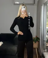 Remera de punto acanalado con escote redondo y cierre frontal parcial con botones. Presenta mangas largas y un ajuste entallado al cuerpo.