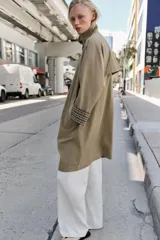 Trench de corte oversize color beige, con cuello alto, cierre frontal de botones y mangas largas con puños vueltos estampados a cuadros. Cuenta con bolsillos delanteros de vivo.