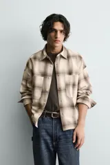 Camisa de algodón con cuello solapa, manga larga y dos bolsillos plastrón en el delantero. Presenta un patrón de cuadros en tonos beige y marrón oscuro.