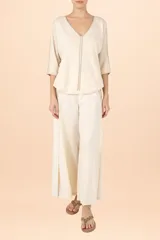 Suéter de punto color crema con cuello en V, mangas tres cuartos y detalle de costura vertical central. Presenta un diseño holgado con terminaciones acanaladas en puños y ruedo.