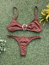 Conjunto de bikini color chocolate con textura acanalada. El corpiño es de estilo triangular con una hebilla metálica decorativa en el centro y breteles finos. La bombacha es de corte colaless con tiras laterales.