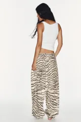 Pantalón de tiro medio con estampado animal print tipo tigre en tonos beige y negro. Presenta trabillas, cintura ajustable con cordones, bolsillos laterales y traseros, y bajo ajustable con cordón. Cierre frontal con cremallera y botón a presión.