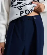 Pantalón de sastrería corte pata ancha, color azul marino, con pliegues delanteros y cierre frontal de doble botón.
