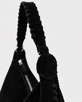 Bolso tipo hobo de gran tamaño, confeccionado en gamuza negra con detalles de costuras artesanales y tientos decorativos en los bordes. Cuenta con un asa trenzada con pespuntes a mano y cierre superior.