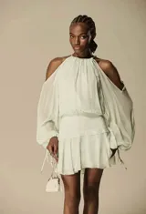 Vestido corto color verde menta claro, con escote halter y hombros descubiertos. Presenta mangas largas amplias y ajustadas en el puño, y un corte fruncido en la cintura que da lugar a una falda corta con volados.