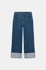 Jeans de tiro alto y corte ancho (wide leg) en denim azul medio. Presenta costuras verticales marcadas en el frente de ambas piernas y puños anchos doblados en el bajo.