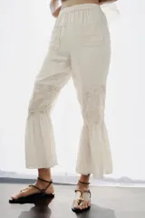 Pantalón de tiro alto con cintura elástica, confeccionado en viscosa. Presenta bolsillos de plastrón en el frente, aplicaciones de puntilla y bordados florales a tono, con bajo acabado en volantes.
