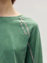 Remera manga larga de algodón color crudo, con cuello redondo y calce holgado. Posee costuras a la vista en color naranja y un delicado bordado con la frase "the flower edit" sobre el hombro izquierdo.