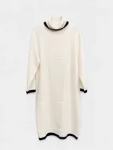 Polera larga de tejido de punto color blanco, con cuello alto y detalles en negro en el cuello, puños y ruedo. Presenta un diseño de corte recto con un tajo frontal vertical.