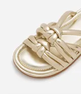 Sandalia plana de color negro con diseño de tiras tubulares acolchadas tipo puffer entrelazadas con nudos. Presenta puntera redonda, plantilla anatómica y suela de goma al tono.