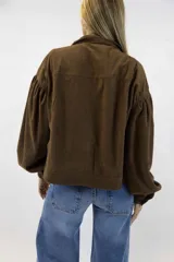 Campera corta de pana color beige, con cuello clásico, cierre frontal con botones y amplios bolsillos con solapa en el pecho. Cuenta con mangas largas abullonadas y diseño holgado.