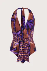 Traje de baño enterizo con diseño halter, escote profundo y estampado botánico en tonos púrpura y marrón cobrizo. Presenta una faja ancha fruncida en la cintura con un lazo decorativo central que cae hacia la parte inferior.