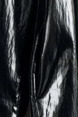 Trench de largo midi con acabado brillante efecto vinilo, manga larga y cuello de solapa en tejido de gamuza a contraste. Presenta cierre frontal con botones ocultos y bolsillos laterales integrados en la costura.