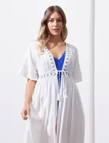 Kaftan largo de playa color blanco, con mangas cortas, escote en V y detalles de puntilla en el frente. Presenta una abertura central con lazo de ajuste en la cintura.