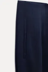 Pantalón blanco de vestir, de tiro alto y corte recto. Presenta bolsillos delanteros de vivo y cierre frontal con cremallera, botón interior y gancho metálico.