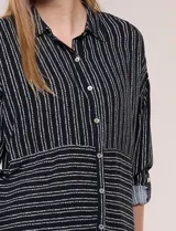 Camisa de rayón negra con patrón de líneas blancas. Presenta cuello camisero, cierre frontal con botones, mangas largas con puños vueltos y un diseño con corte horizontal que alterna líneas verticales en la parte superior y horizontales en la inferior.