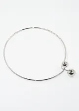 Gargantilla rígida dorada con dos esferas decorativas, una más grande que la otra, unidas por una barra vertical.