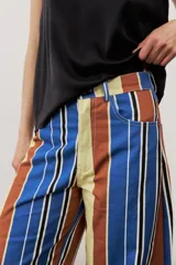 Pantalón de corte ancho y relajado con rayas verticales multicolor en tonos azul, marrón, amarillo, blanco y negro.